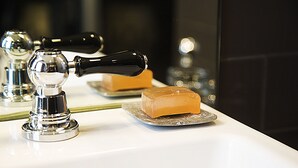Un lavamanos con grifo de cromo, una pastilla de jabón y un espejo que refleja el grifo y el jabón.
