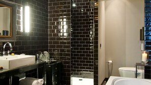 Un baño moderno con pared de azulejos negros, una bañera blanca y un tocador con doble lavabo.
