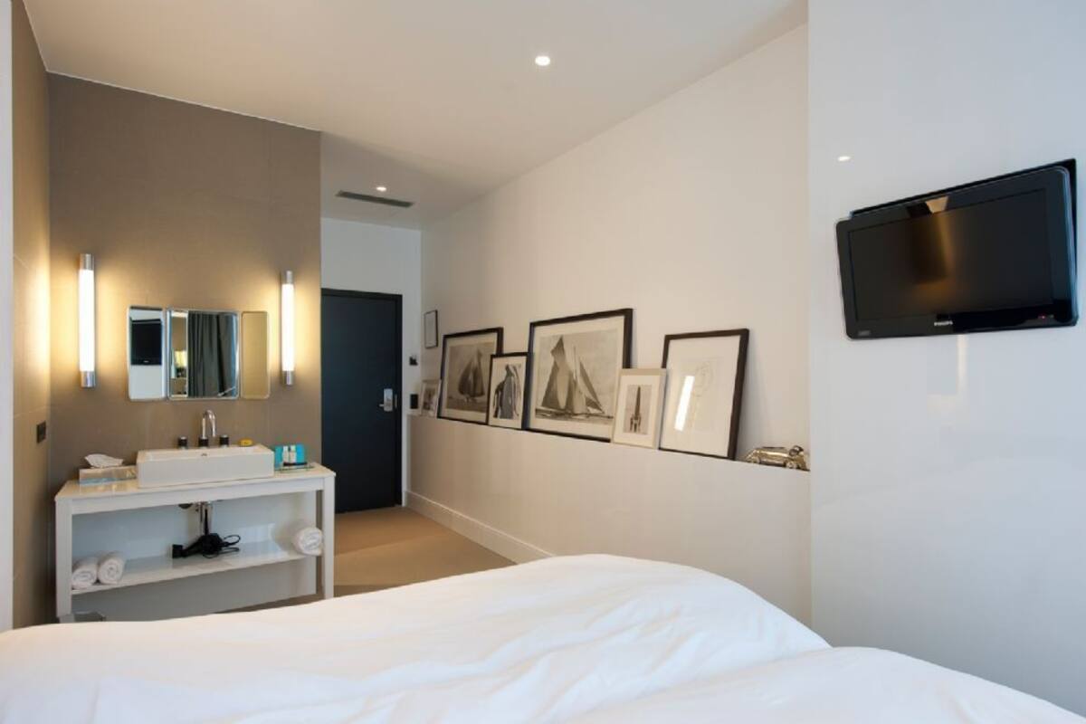 Quarto de hotel com cama, penteadeira com espelho, televisão de tela plana na parede e quadros decorativos na parede.