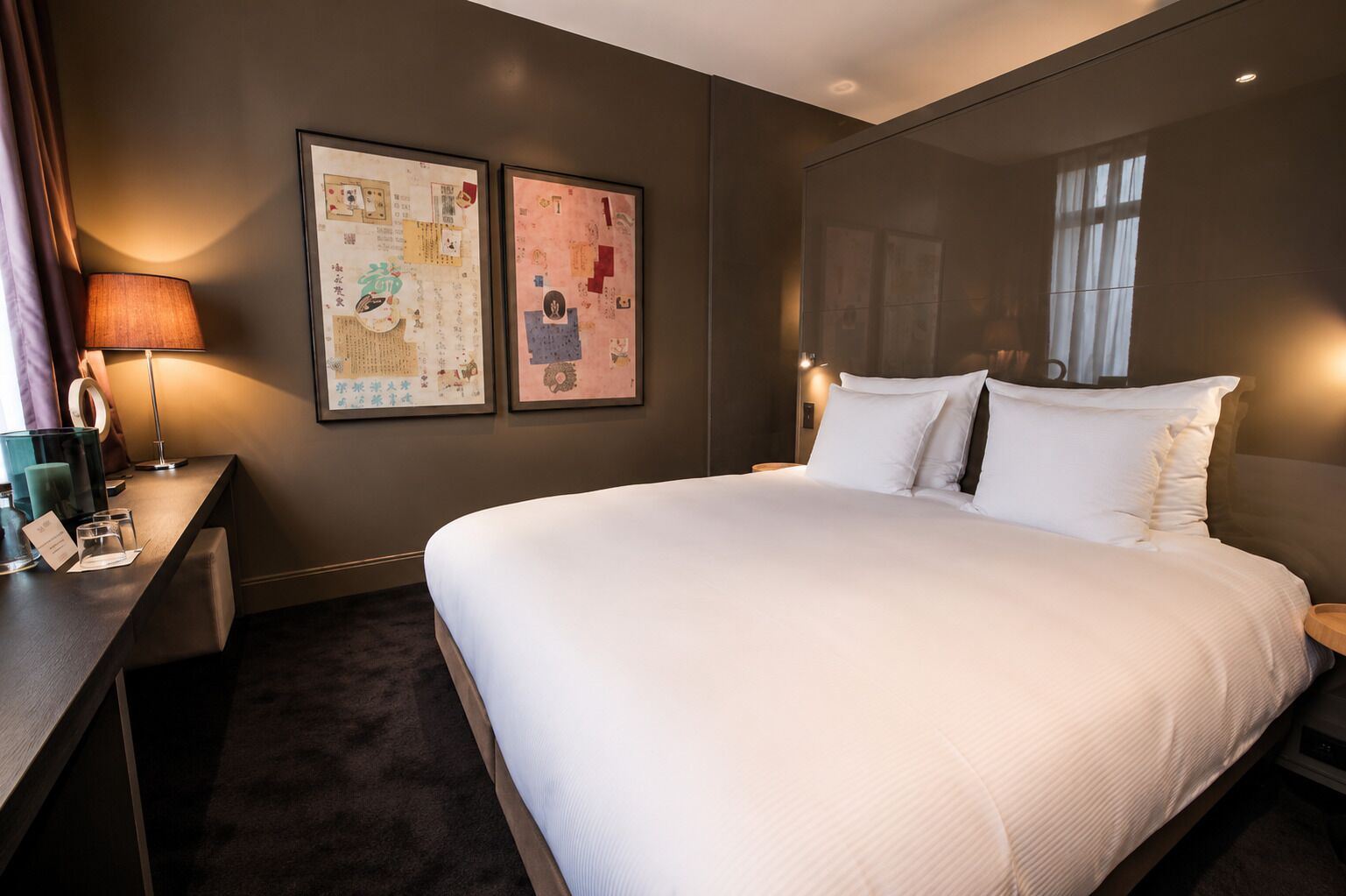 Habitación de hotel con una cama grande, un escritorio con lámpara y dos cuadros en la pared.