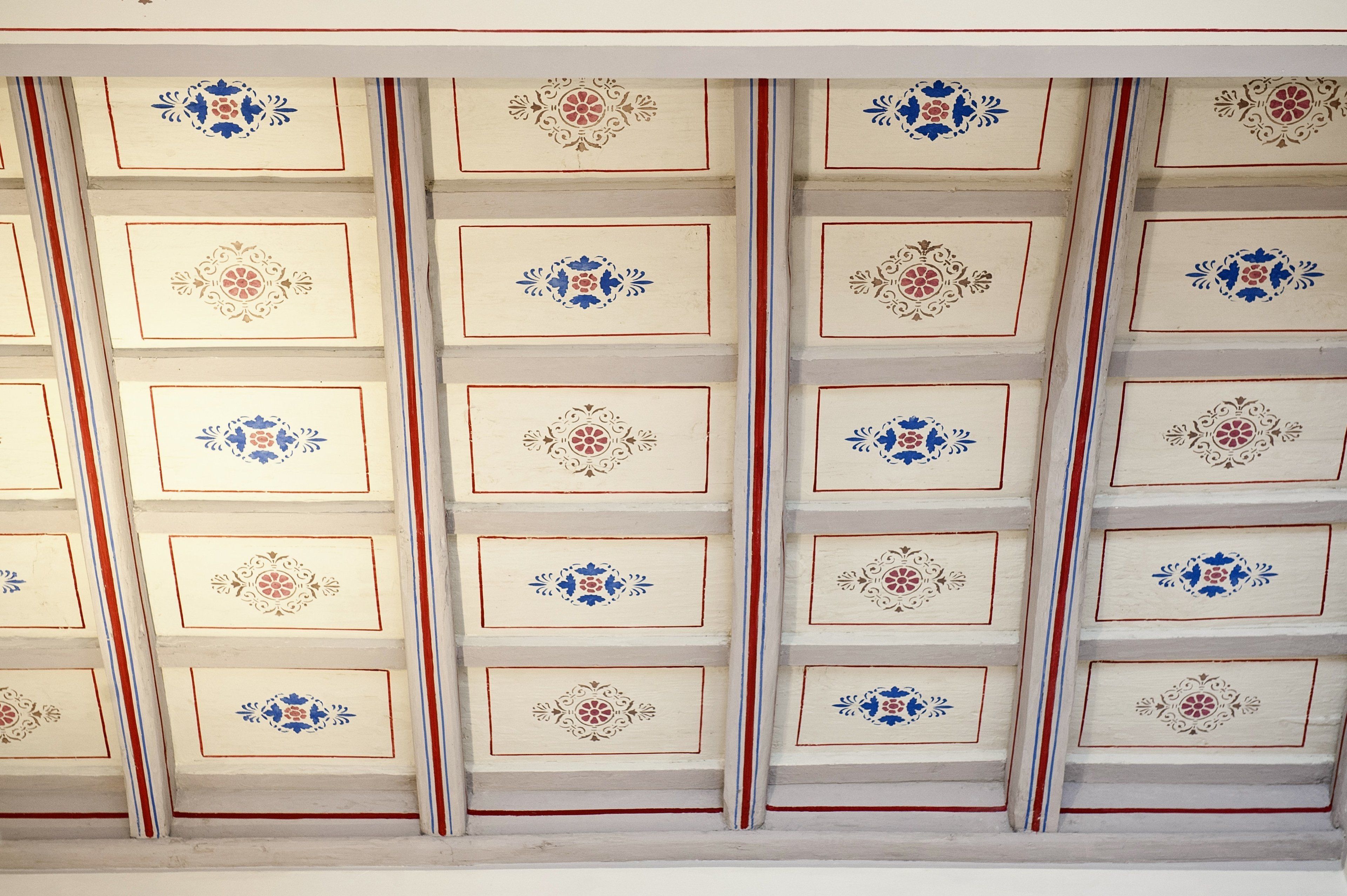 Un plafond orné d’un réseau de panneaux décoratifs, chacun présentant un motif floral central.