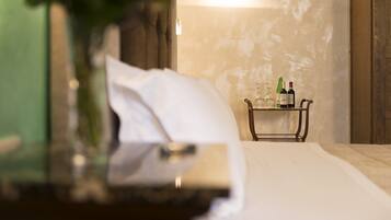A neatly made bed with a white pillow and a bedside table with a bottle and glasses.