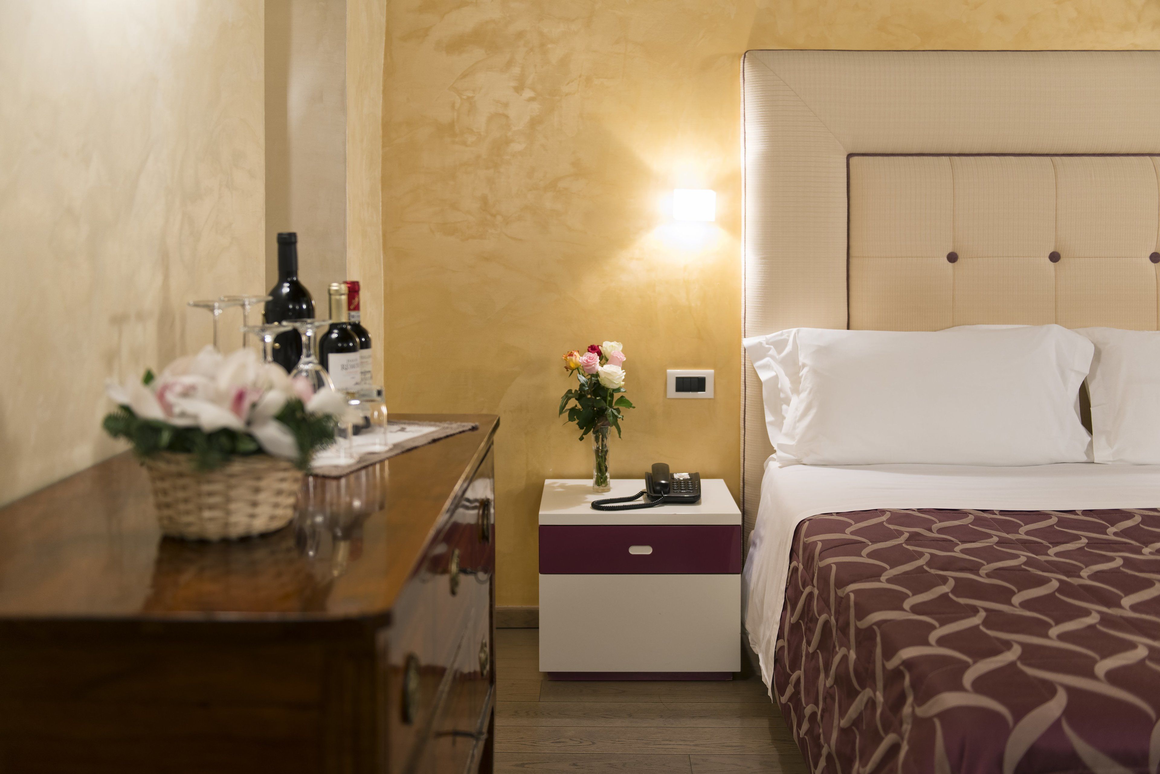 Une chambre d’hôtel avec un lit, une table de chevet et une petite table de nuit ornée d’un vase de fleurs.