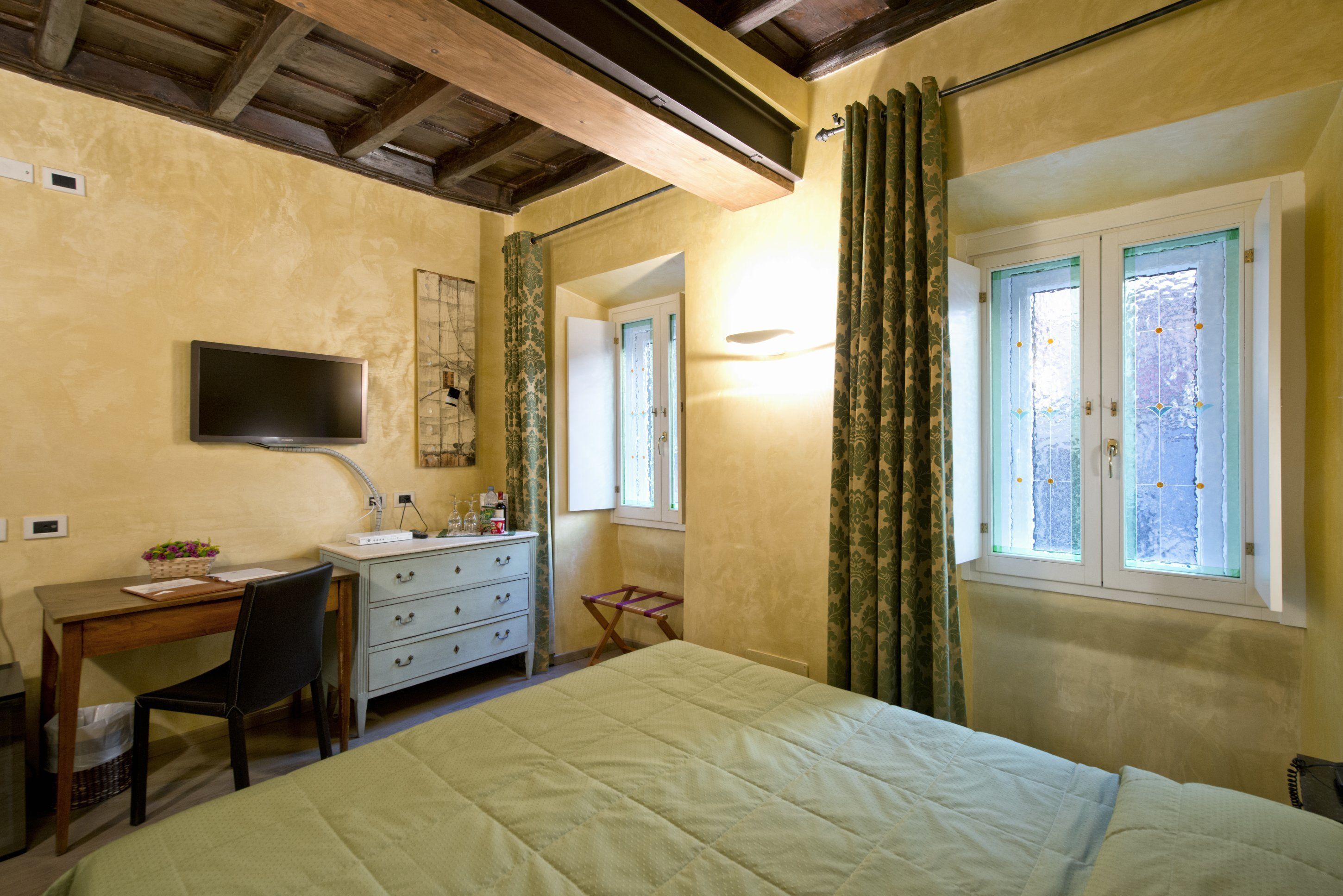 A bedroom with a bed, a desk, a chair, a dresser, a television, and a window with curtains.