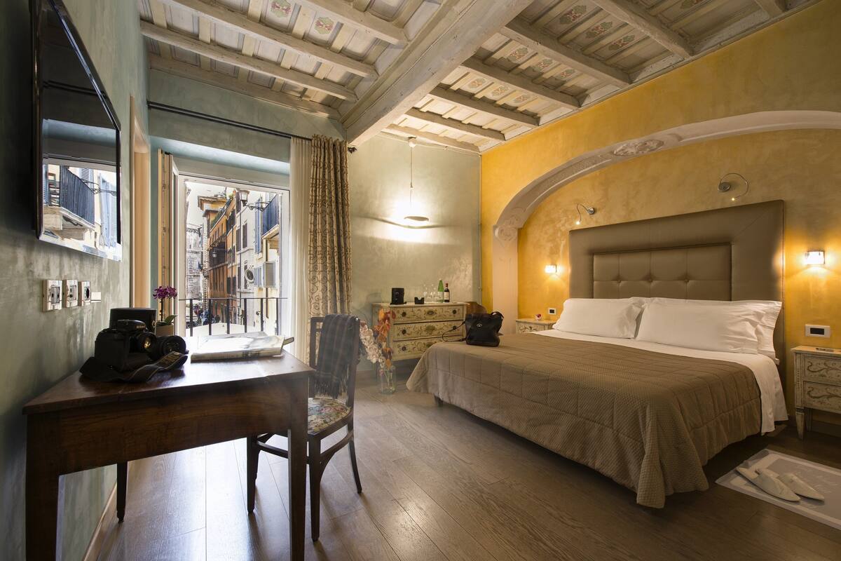 A hotel room with a bed, a desk, a chair, a dresser, and a view of the outside.