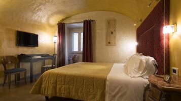 Ein Hotelzimmer mit einem Bett, einem Schreibtisch, einem Sessel, einem Fernseher und einer Uhr auf einem Nachttisch.