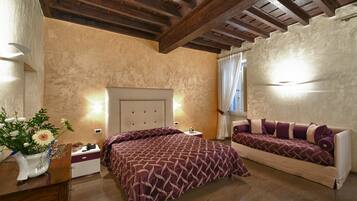 A bedroom with a bed, a sofa, a nightstand, and a vase with flowers.