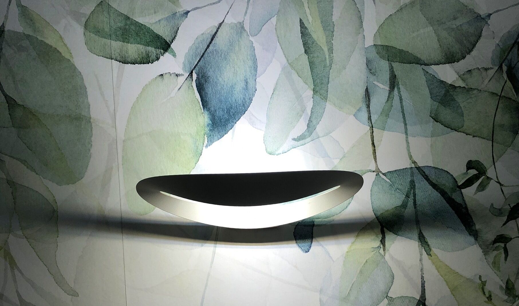 A wall with a minimalist light fixture and a watercolor leaf pattern.