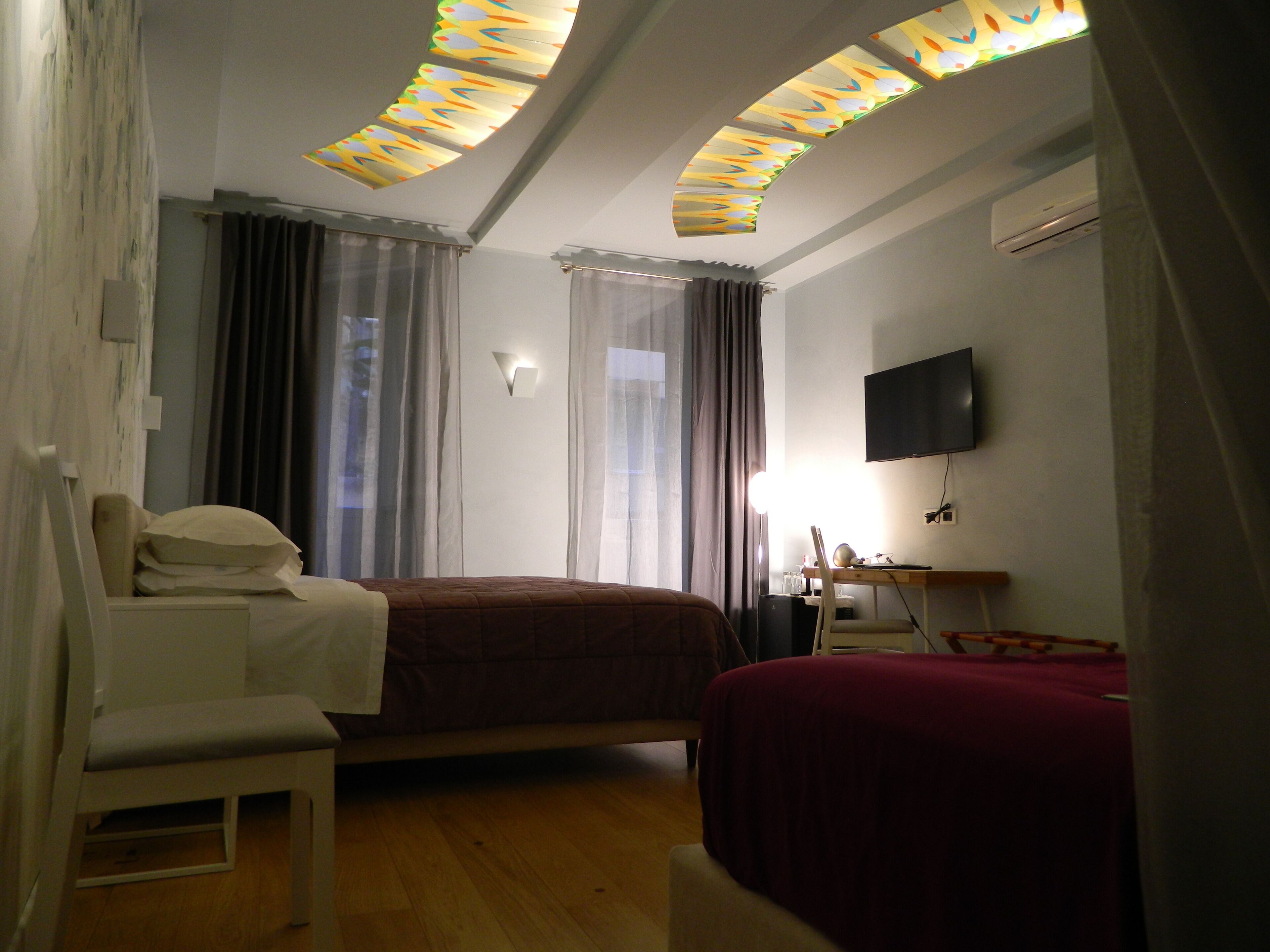 A hotel room with a bed, a desk, a chair, a TV, and a ceiling with skylights.