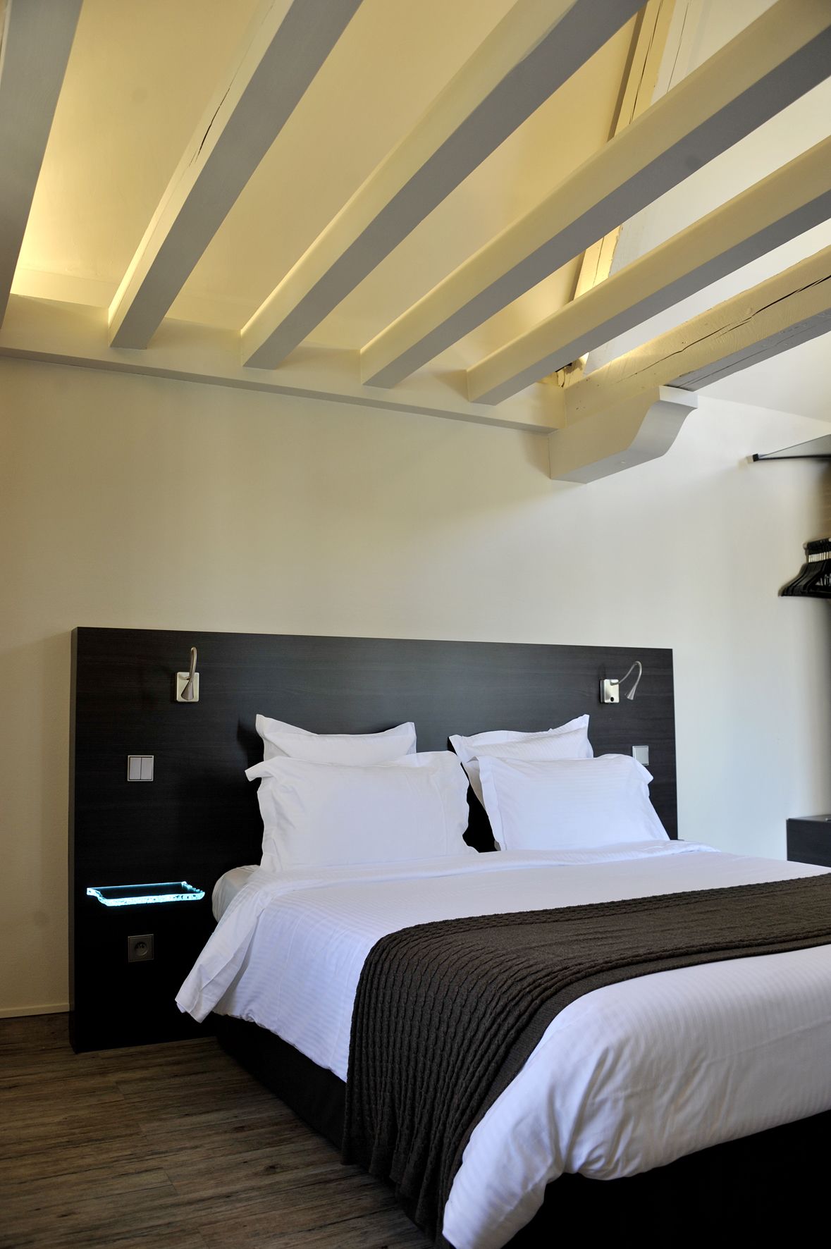 Ett modernt hotellrum med en stor säng, en mörk sänggavel och ett träpanelat tak.