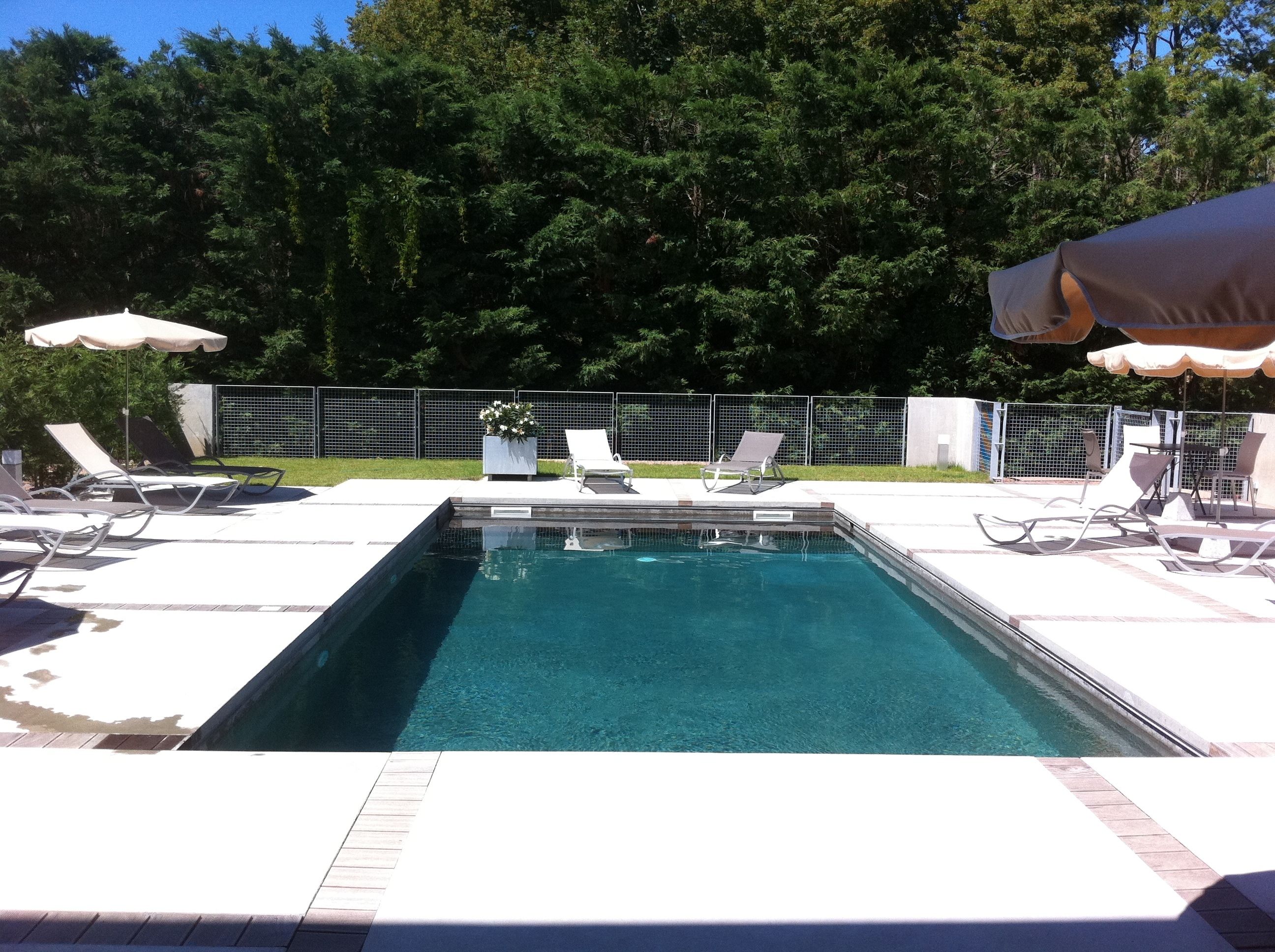 A rectangular swimming pool with clear blue water, surrounded by white lounge chairs and umbrellas.