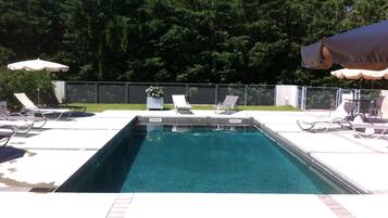 A rectangular swimming pool with clear blue water, surrounded by white lounge chairs and umbrellas.
