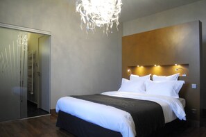 Une chambre d’hôtel moderne avec un grand lit, un dressing et un lustre.