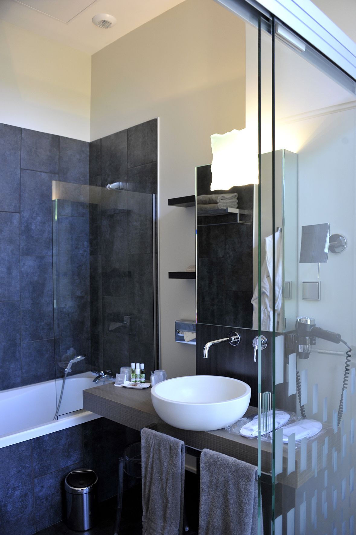 Un baño moderno con una amplia ducha de vidrio, un lavamanos blanco y un cabezal de ducha manual.