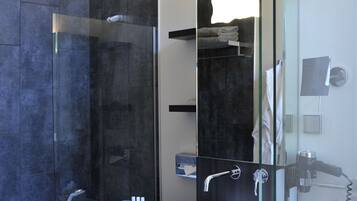 Un baño moderno con una amplia ducha de vidrio, un lavamanos blanco y un cabezal de ducha manual.