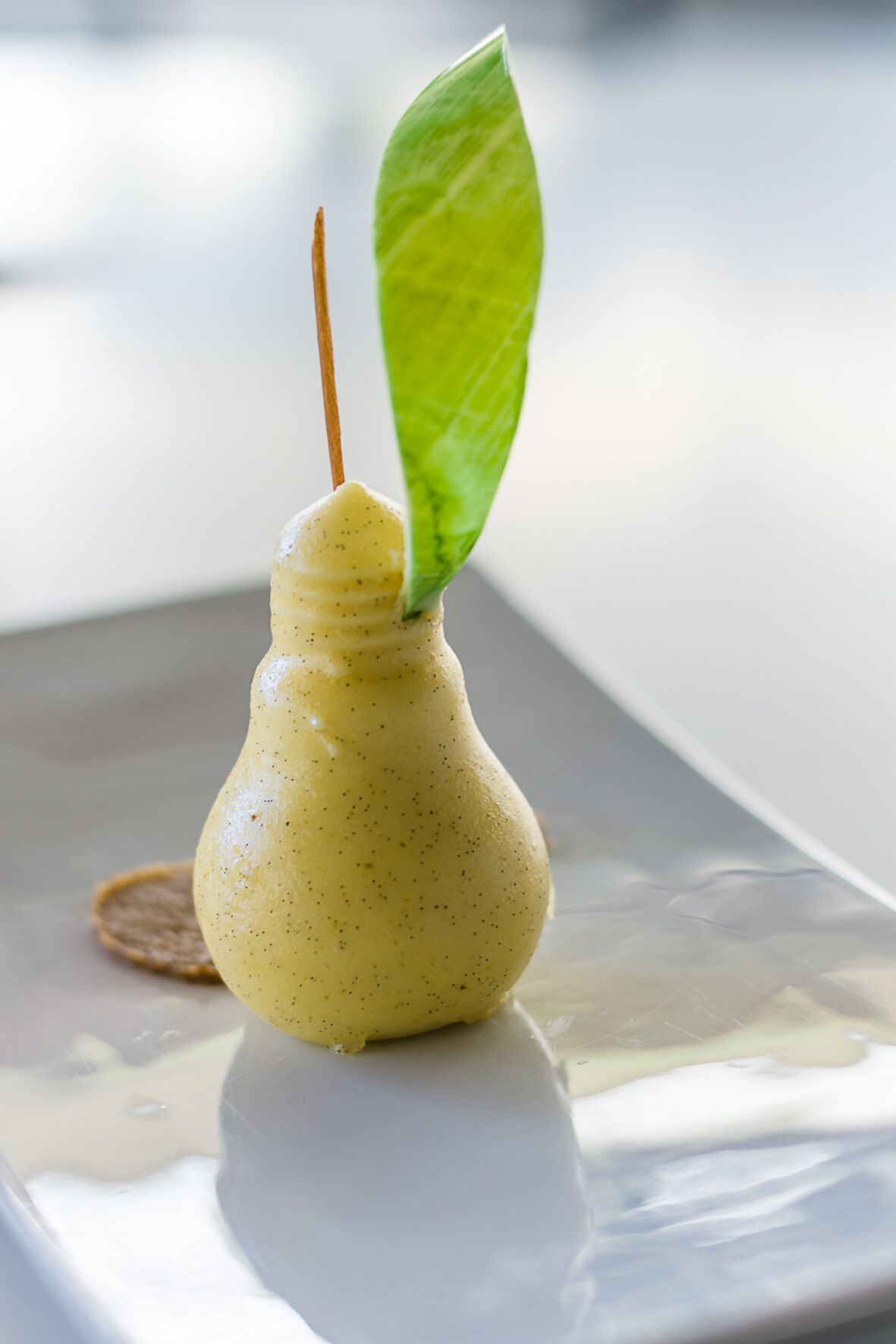 Un postre en un molde con forma de bombilla, con una hoja verde encima, sobre una superficie reflectante.