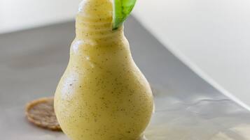 Un postre en un molde con forma de bombilla, con una hoja verde encima, sobre una superficie reflectante.