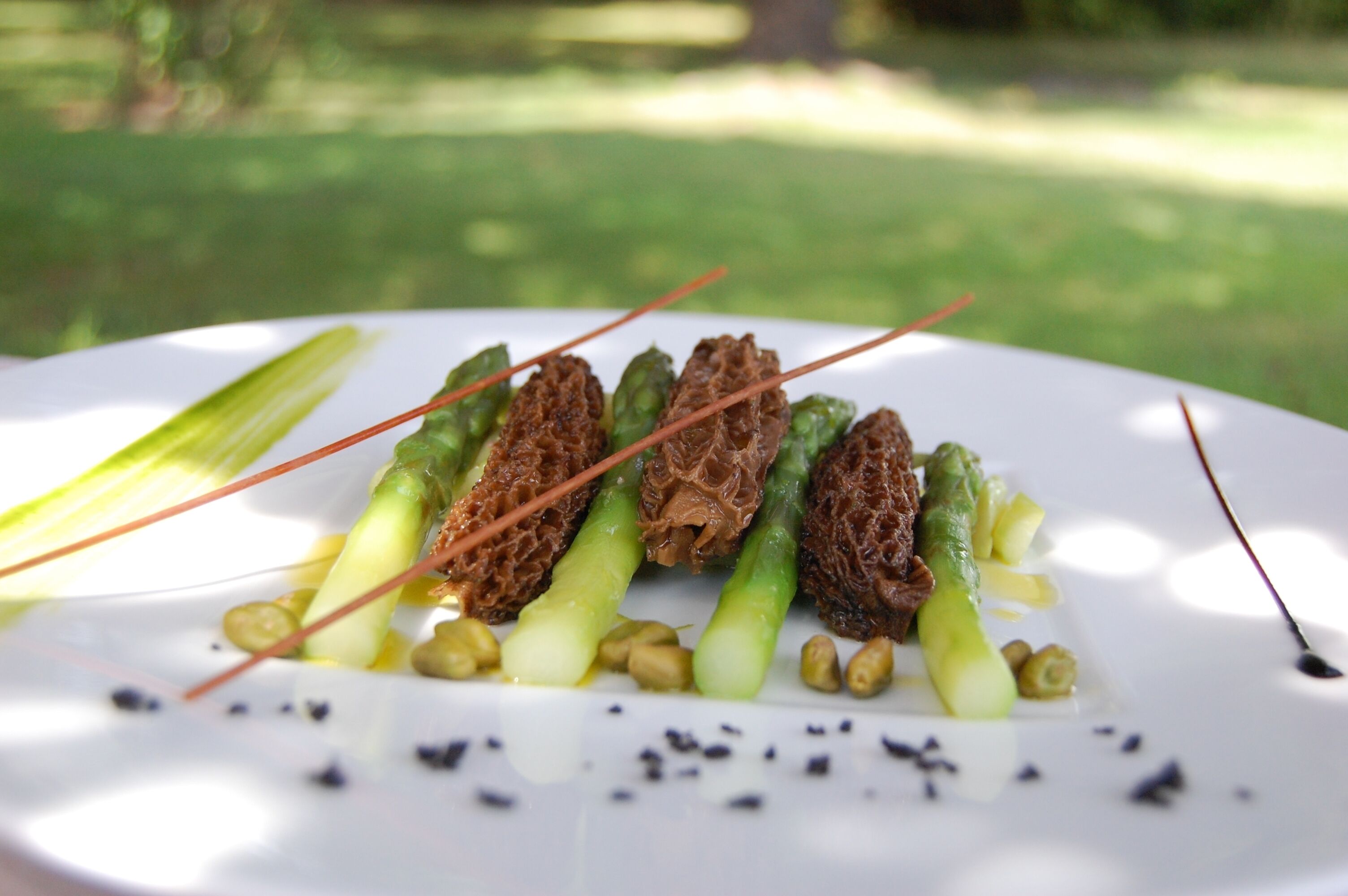 A white plate with a dish of asparagus and other vegetables, garnished with black pepper and a drizzle of sauce.
