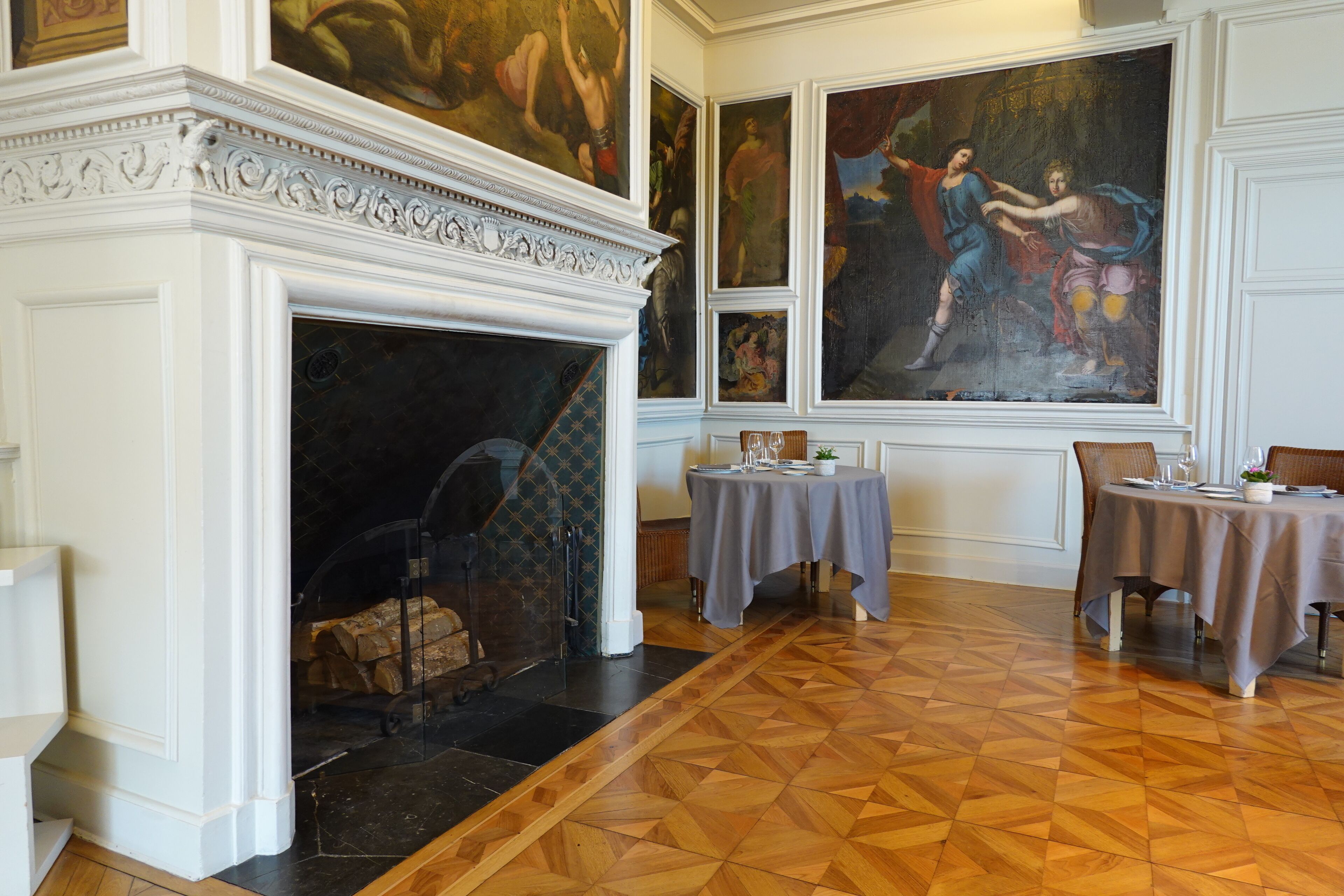 Una habitación con chimenea, un comedor con dos mesas y un cuadro grande en la pared.