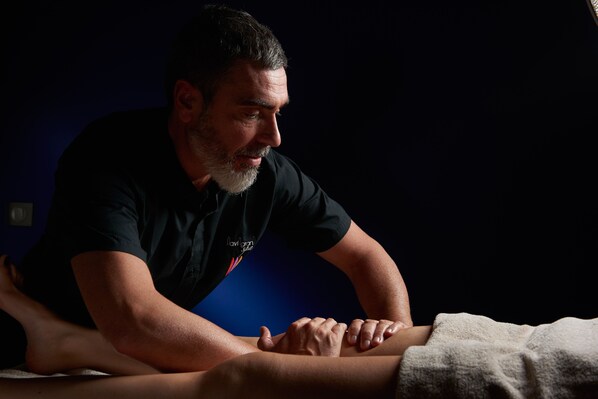 A person performing a massage on another individual in a dimly lit room.
