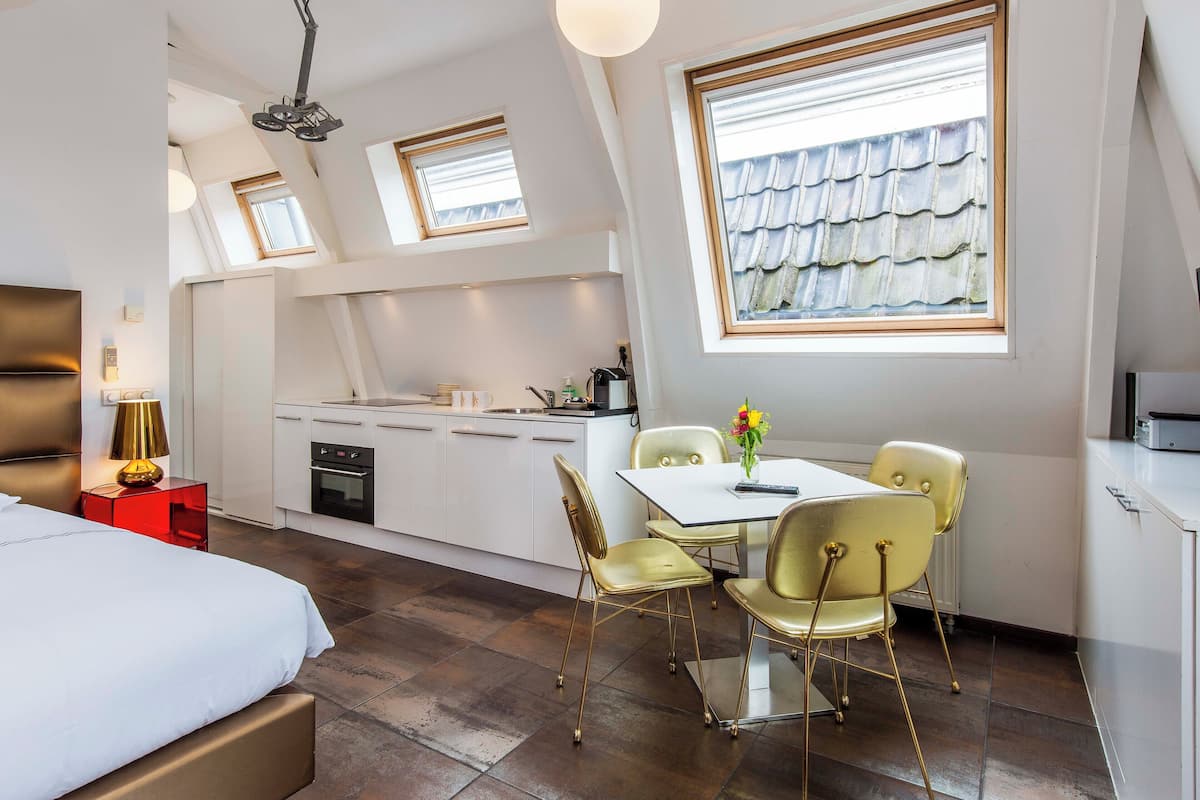 A modern bedroom with a large bed, a small kitchen area, and a dining table with chairs.