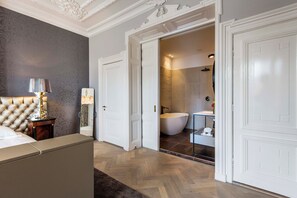 Une chambre à coucher avec une tête de lit capitonnée, une table de chevet avec une lampe et un grand miroir.