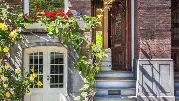 A brick building with a white door, a wooden door with a decorative design, and a sign with the number 16. - Amstel Corner Hotel (Amsterdam)