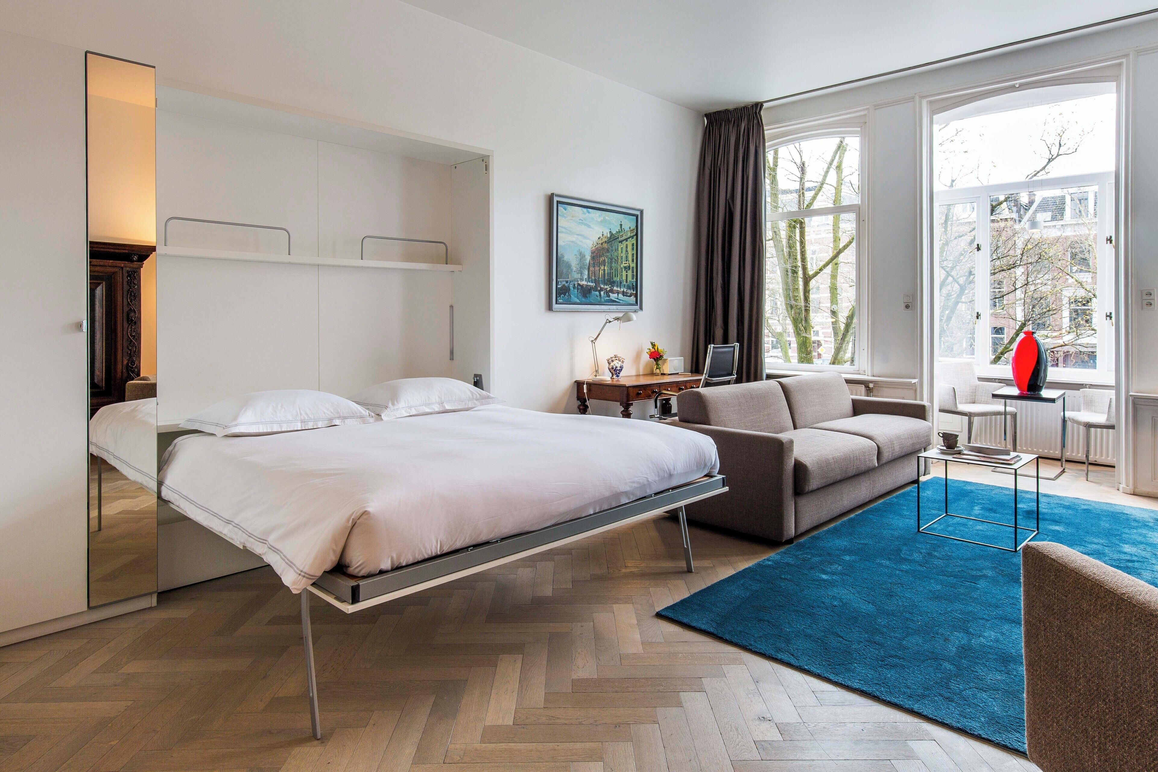 A hotel room with a bed, a sofa, a desk, and a large window.