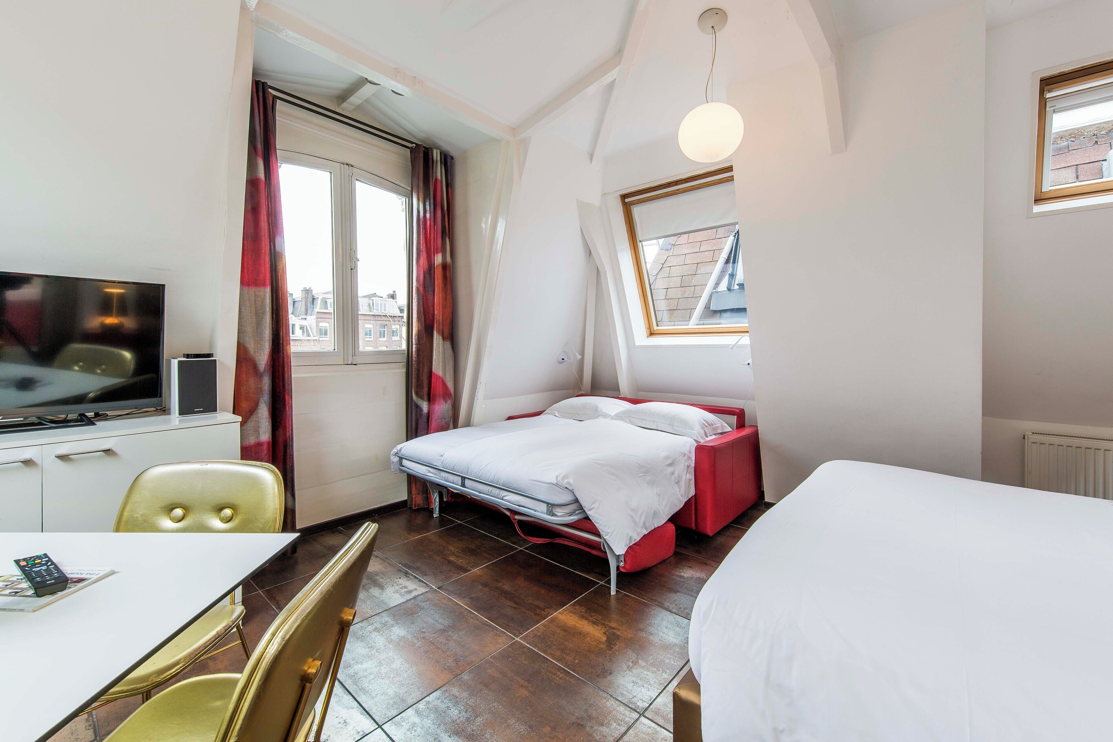 Une chambre d’hôtel de taille réduite, comprenant un lit, un bureau avec une chaise, un téléviseur et une fenêtre avec des rideaux.