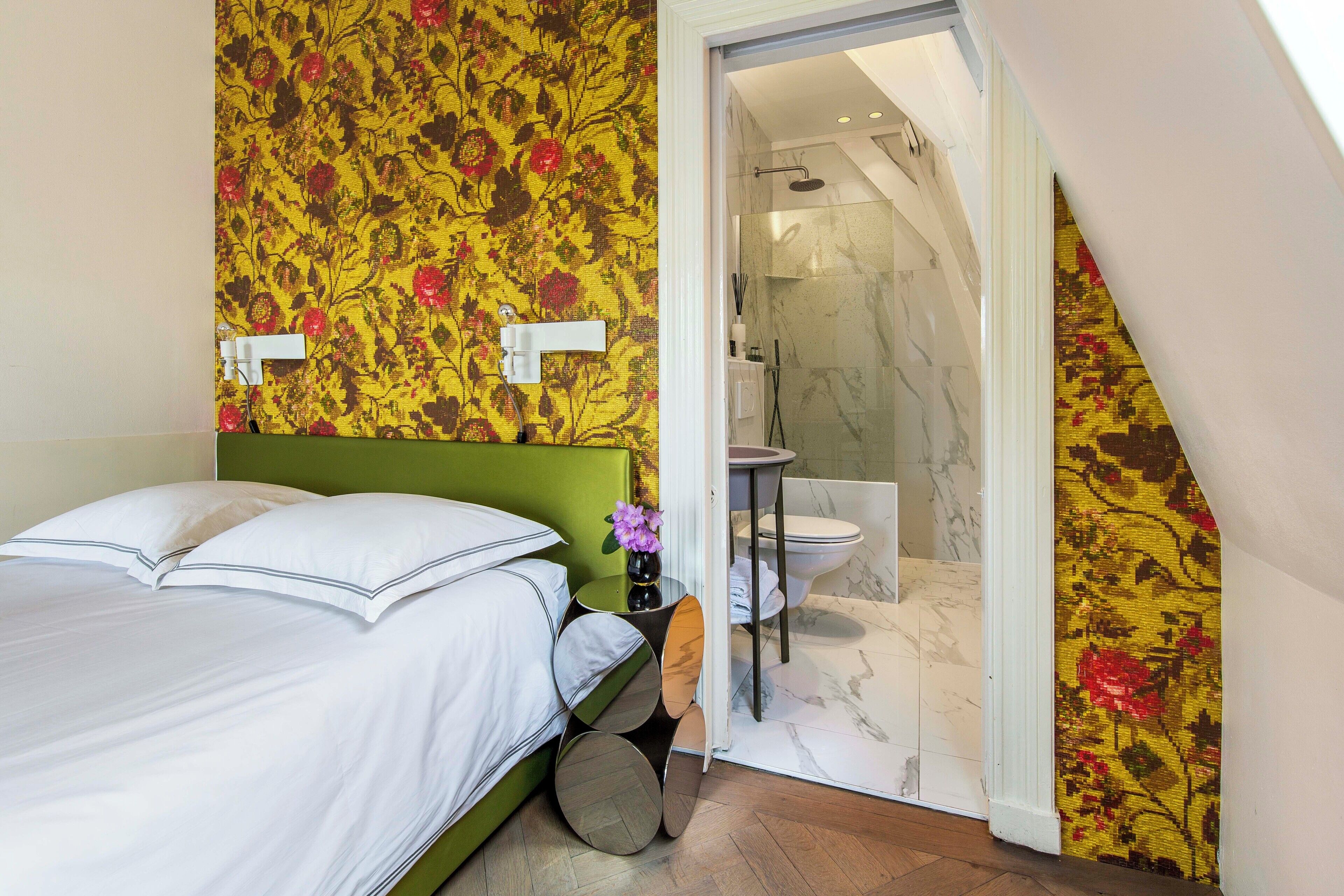 A bedroom with a green headboard, a bed with white bedding, a round mirror, and a small table with a vase of flowers.