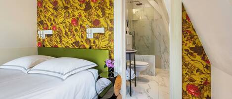 A bedroom with a green headboard, a bed with white bedding, a round mirror, and a small table with a vase of flowers.