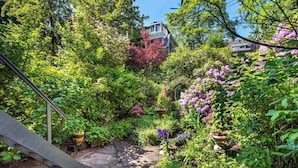 A garden pathway leading to a traditional house surrounded by lush greenery and flowering plants. - Amstel Corner Hotel (Amsterdam)