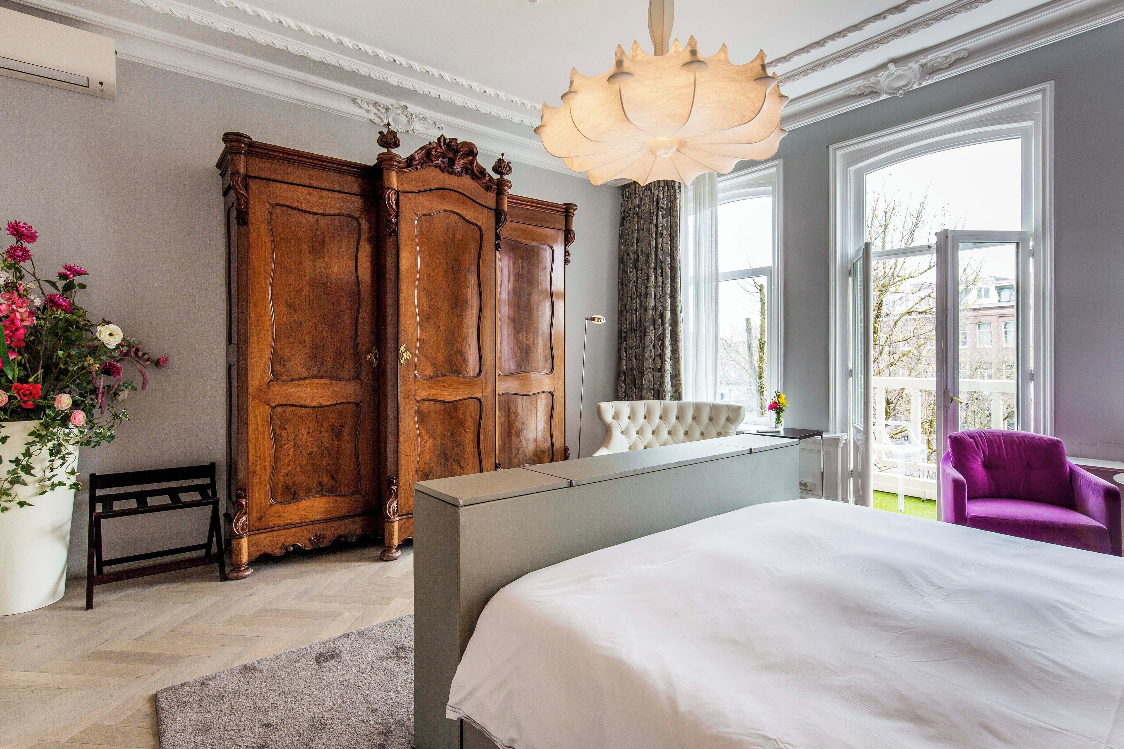 A bedroom with a large bed, a wooden wardrobe, a white bench, and a purple chair.