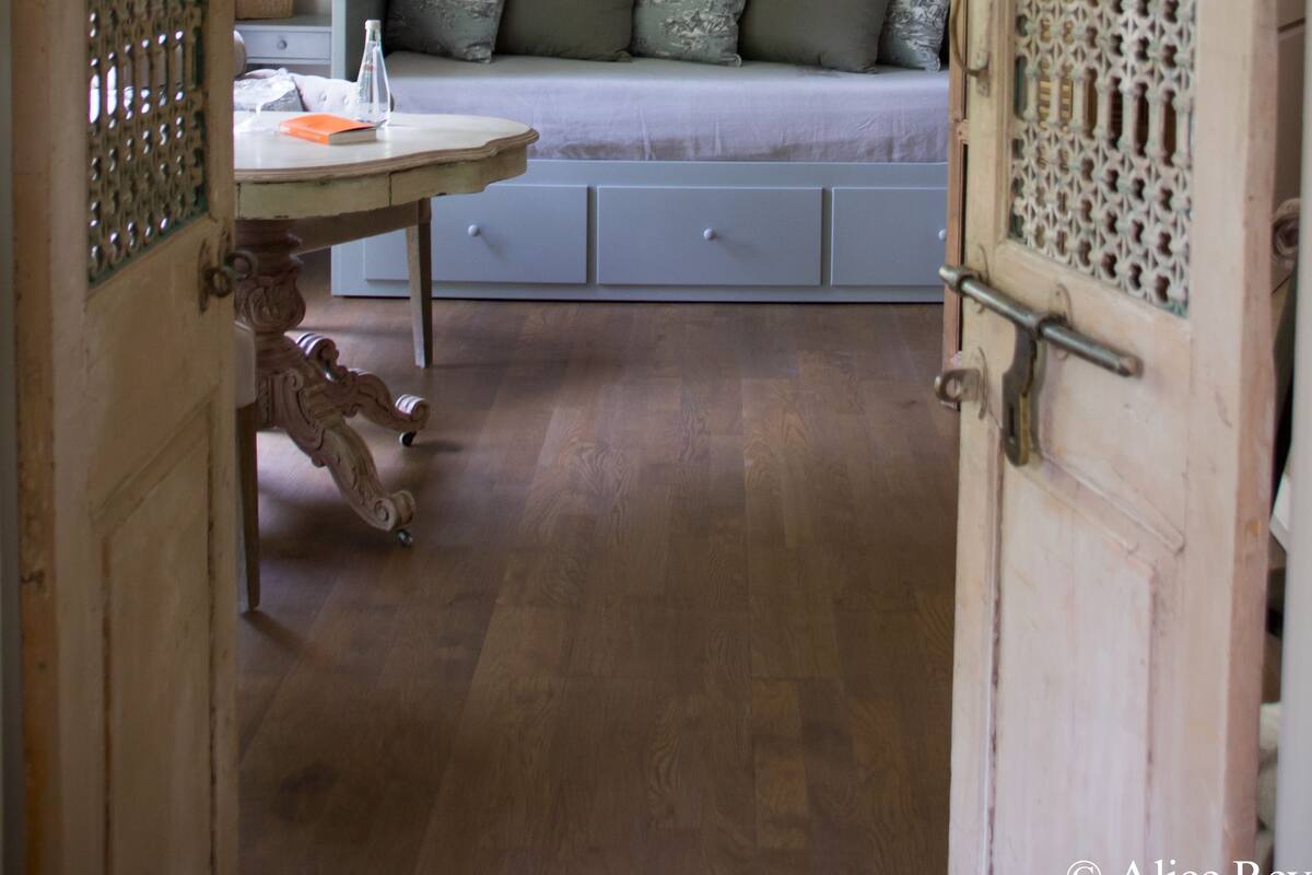 A bedroom with a bed, a bedside table, a mirror, and a wooden door with intricate carvings.