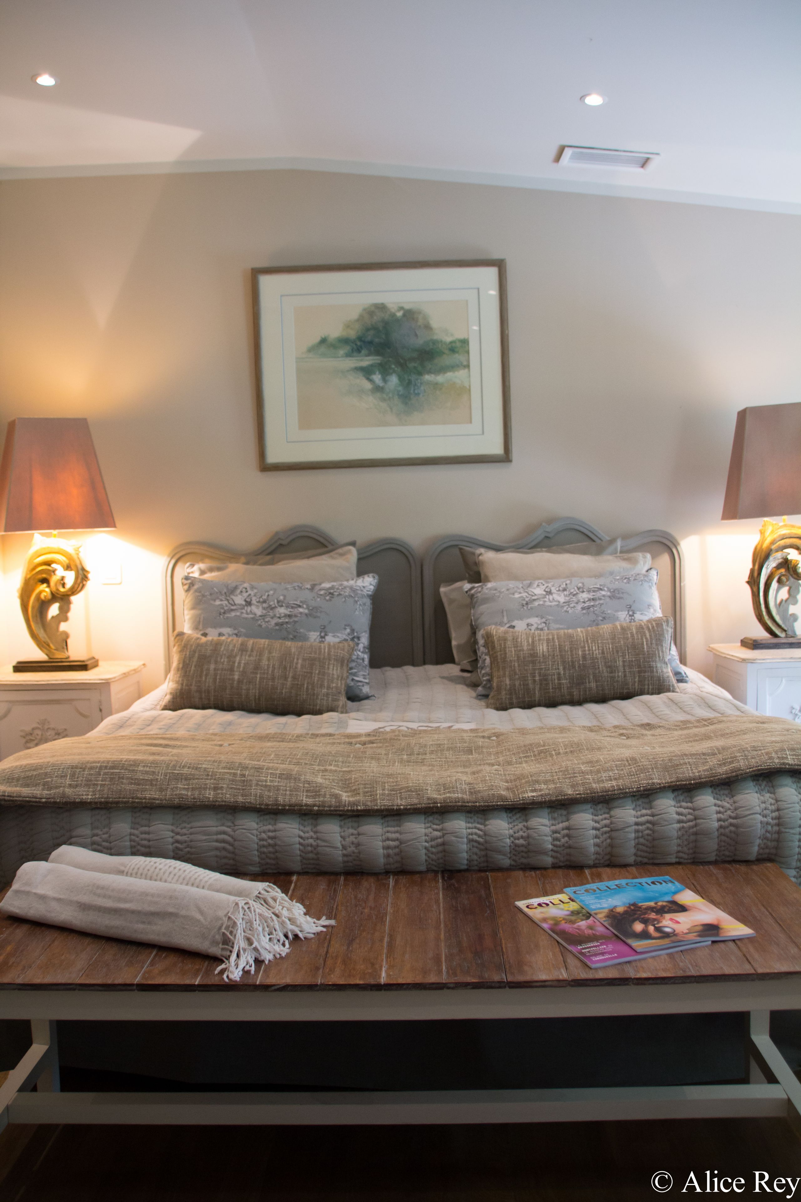 A neatly made bed with a quilt, pillows, and a magazine on a wooden bedside table.