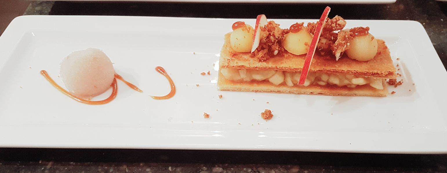 Un dessert servi dans une assiette blanche, nappé d’un filet de caramel et accompagné d’une boule de glace.