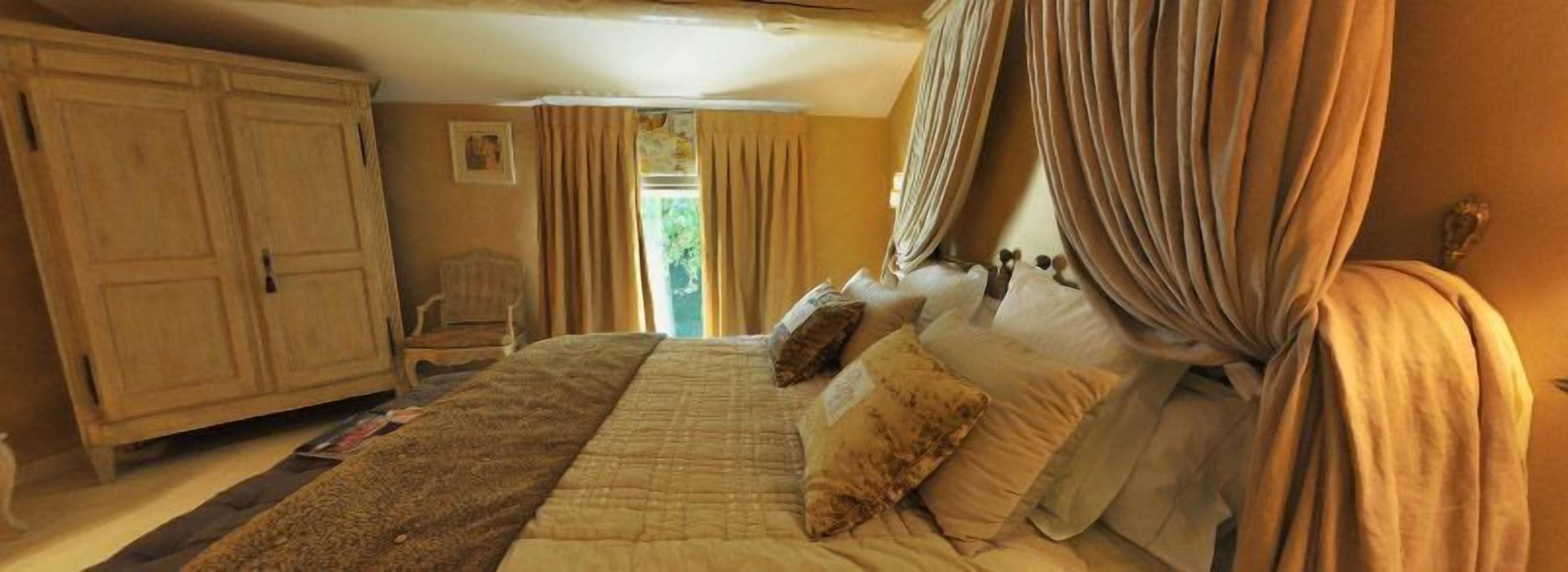 A bedroom with a large bed, curtains, a wooden wardrobe, and a chair.