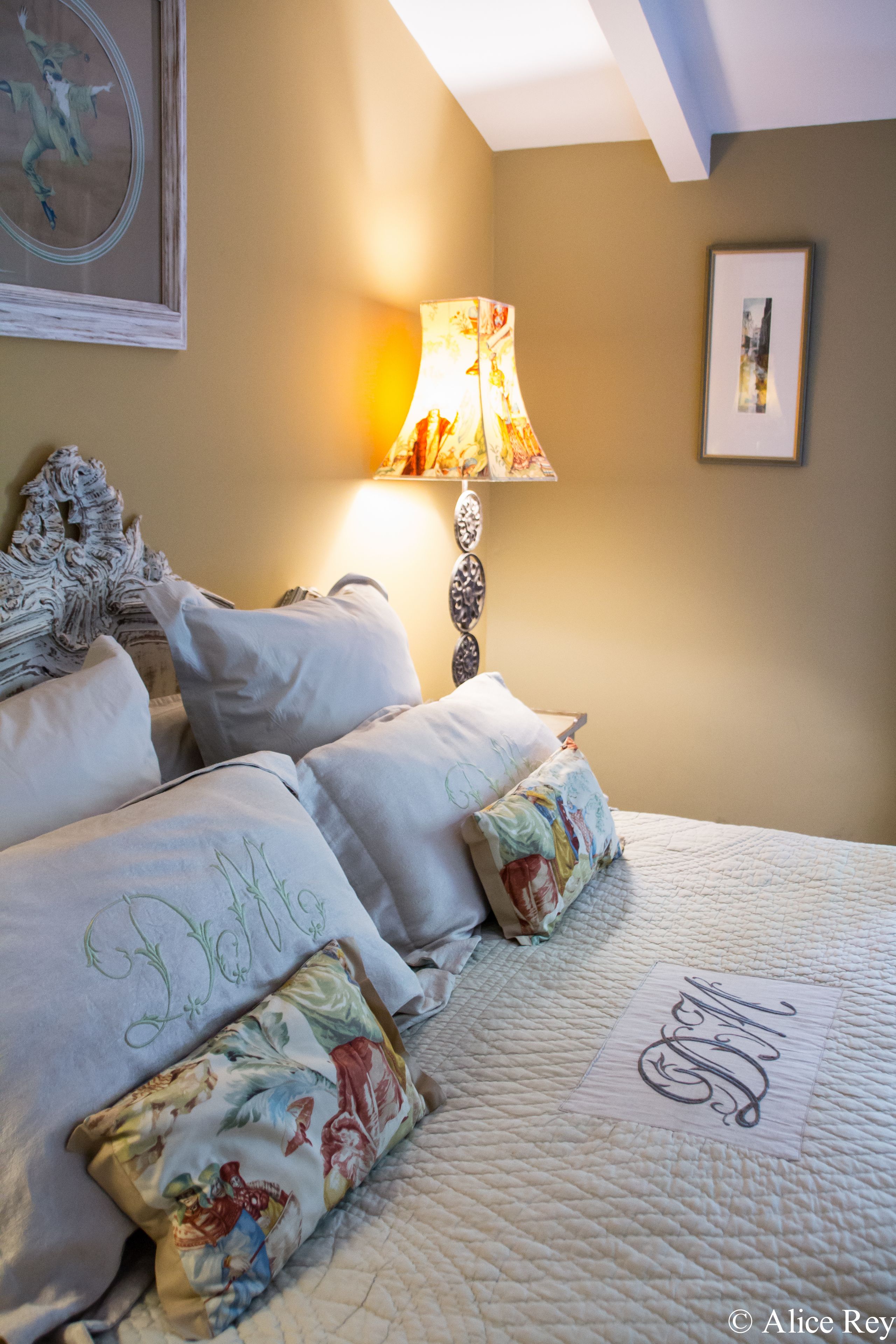 Een net opgemaakt bed met decoratieve kussens en een quilt met monogram.