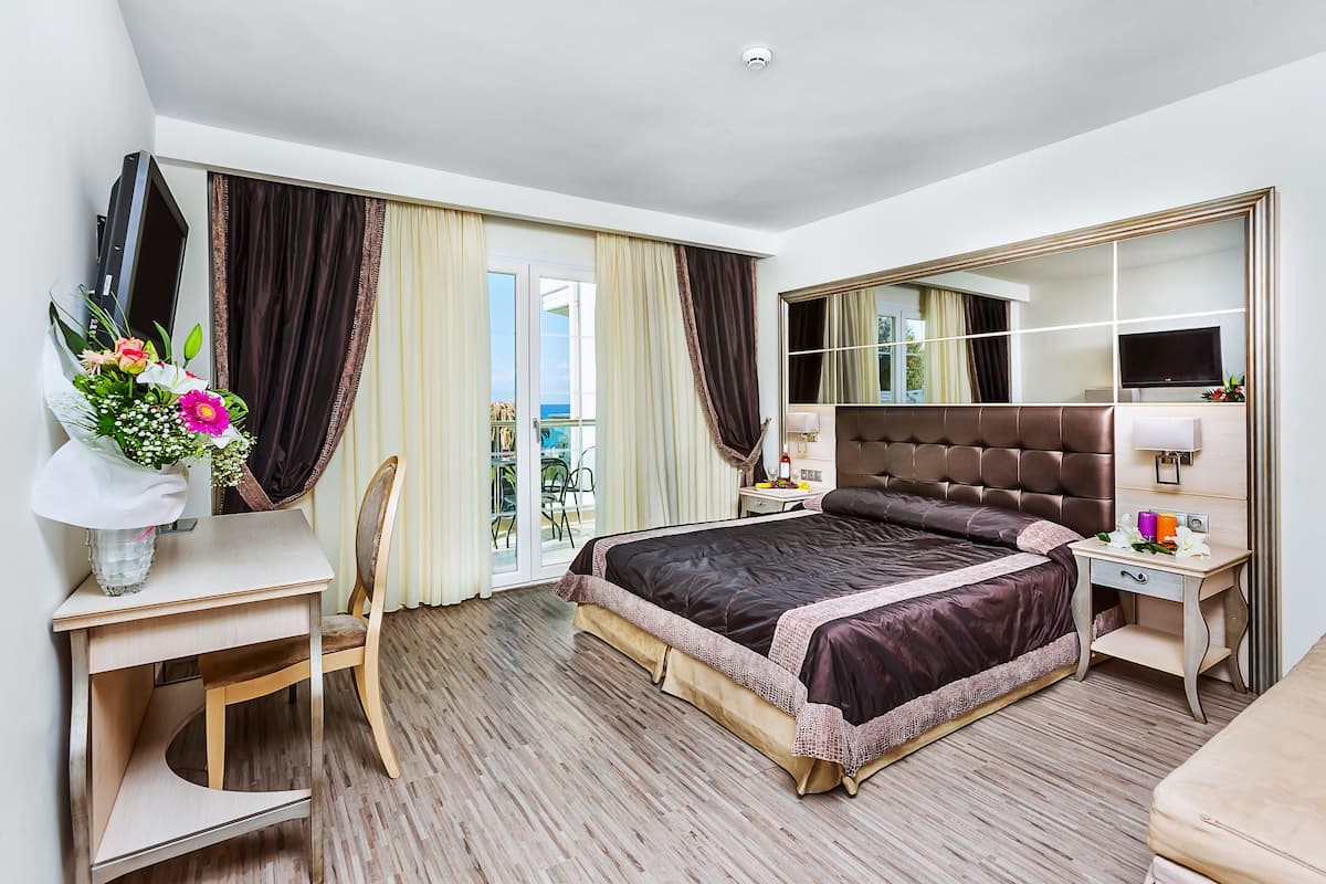 Una habitación de hotel con una cama grande, un escritorio con silla, un televisor y un espejo.