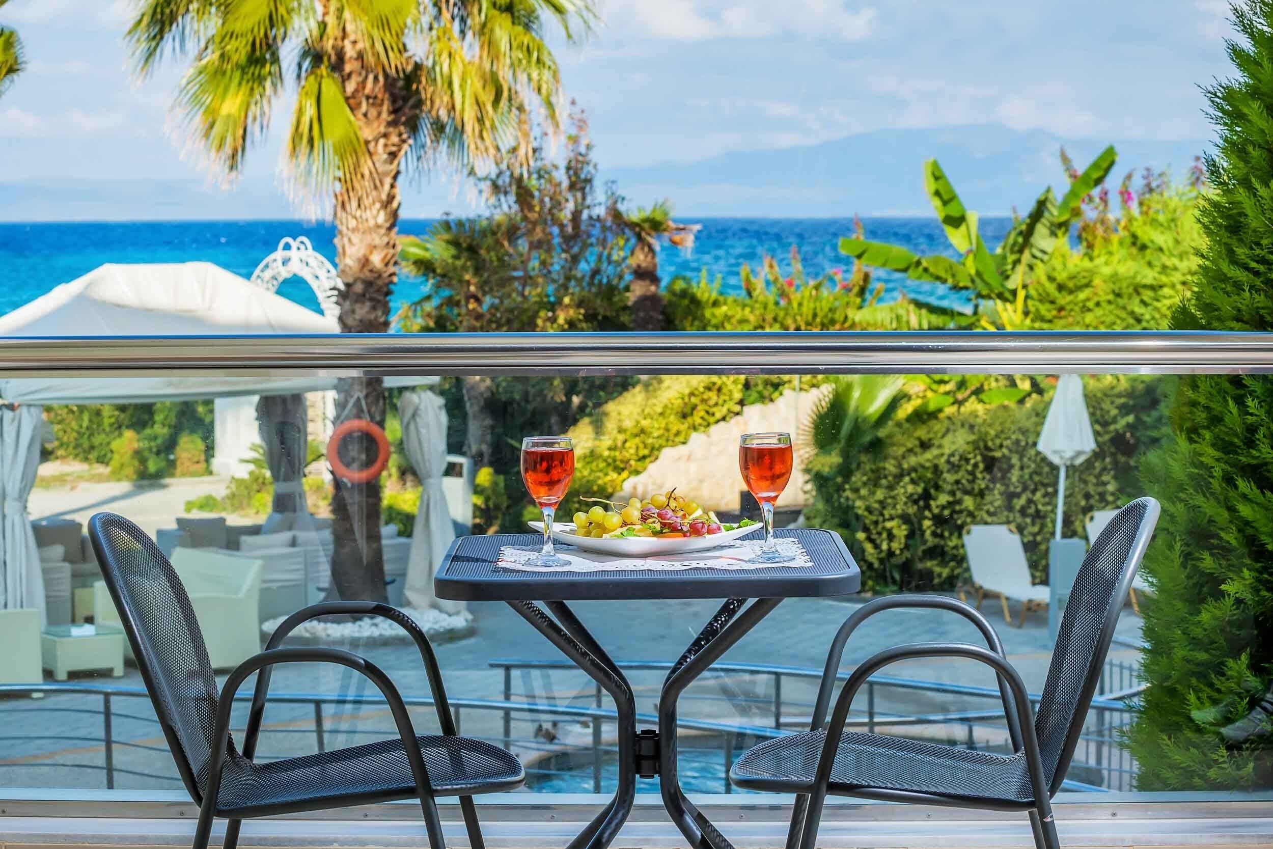 A dining table with two chairs, a plate of food, and two glasses of red wine, overlooking a pool and a scenic ocean view.