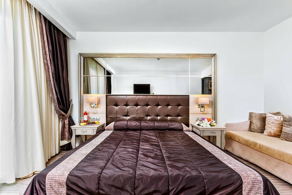 Una habitación de hotel con una cama grande, un sofá, un televisor y un espejo.
