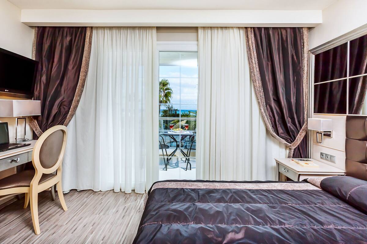 Una habitación de hotel con una cama, un escritorio, un televisor y un balcón con mesa y sillas.