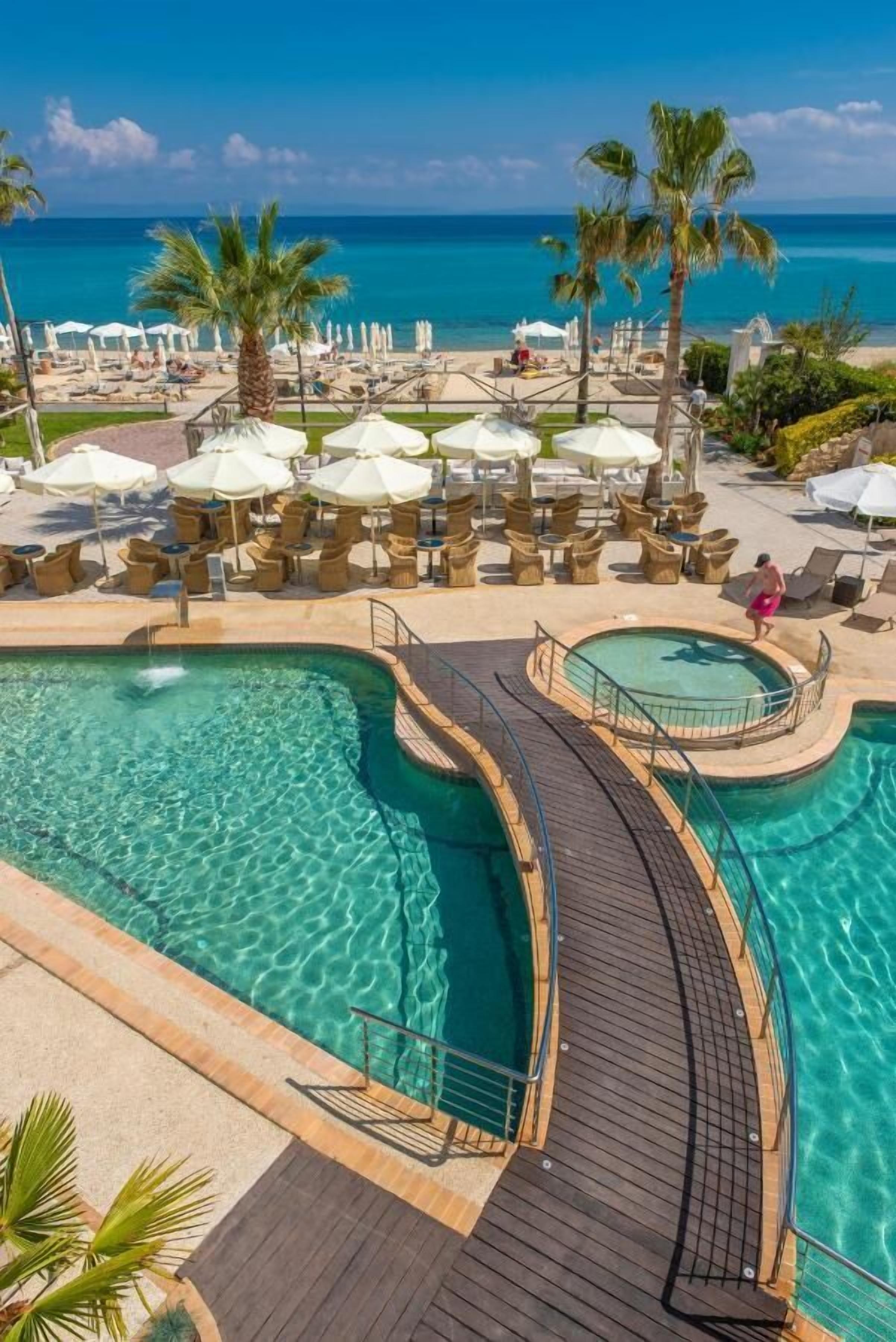 A resort pool area with clear water, lounge chairs, umbrellas, and a view of the ocean.