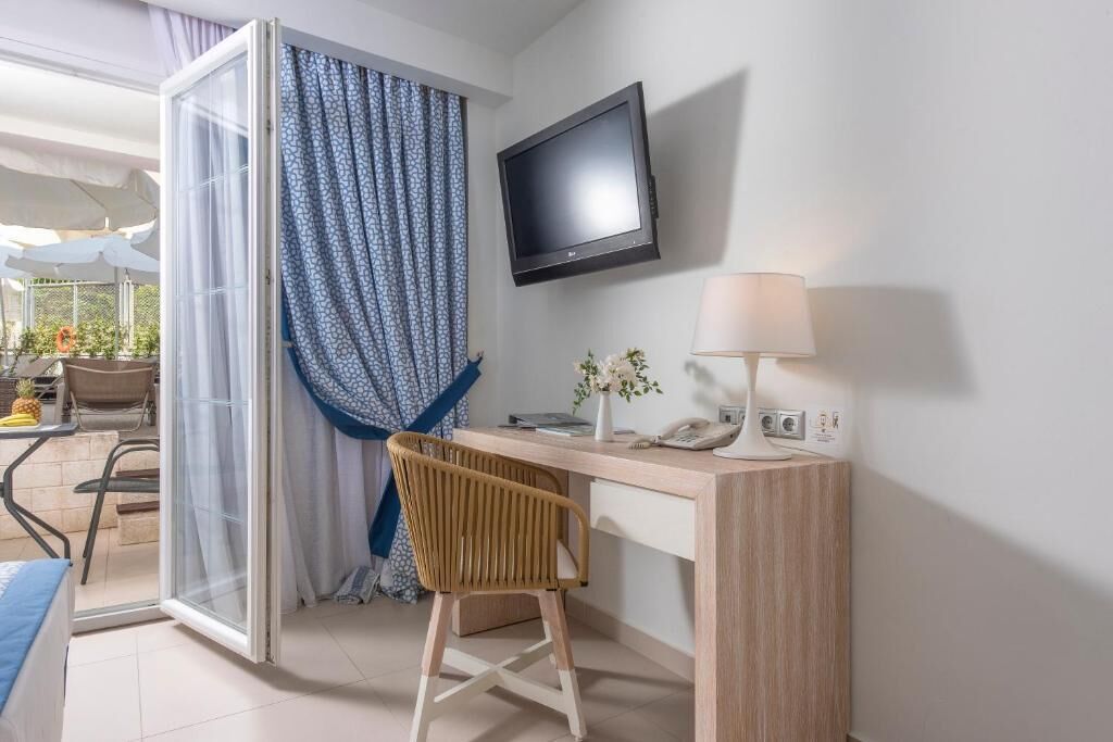 Una habitación de hotel moderna con escritorio, silla, televisor y vista al patio exterior.