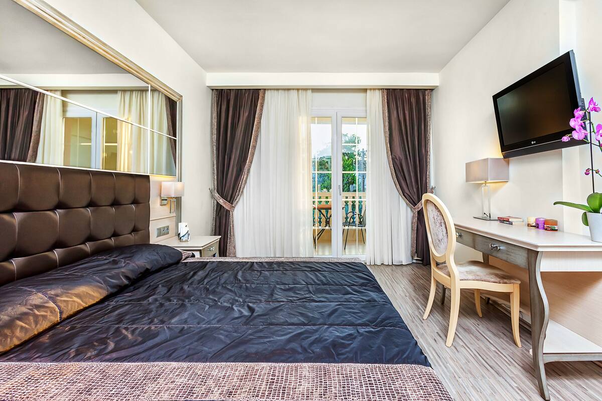 Habitación de hotel con una cama grande, un escritorio, una silla, un televisor y vistas al balcón.