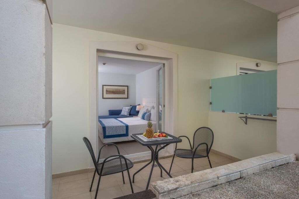A small room with a bed, a table with fruit, and two chairs.