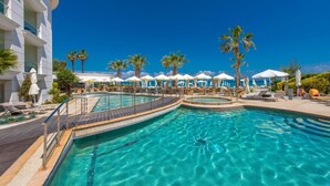 A swimming pool with lounge chairs and umbrellas, surrounded by palm trees and a building.