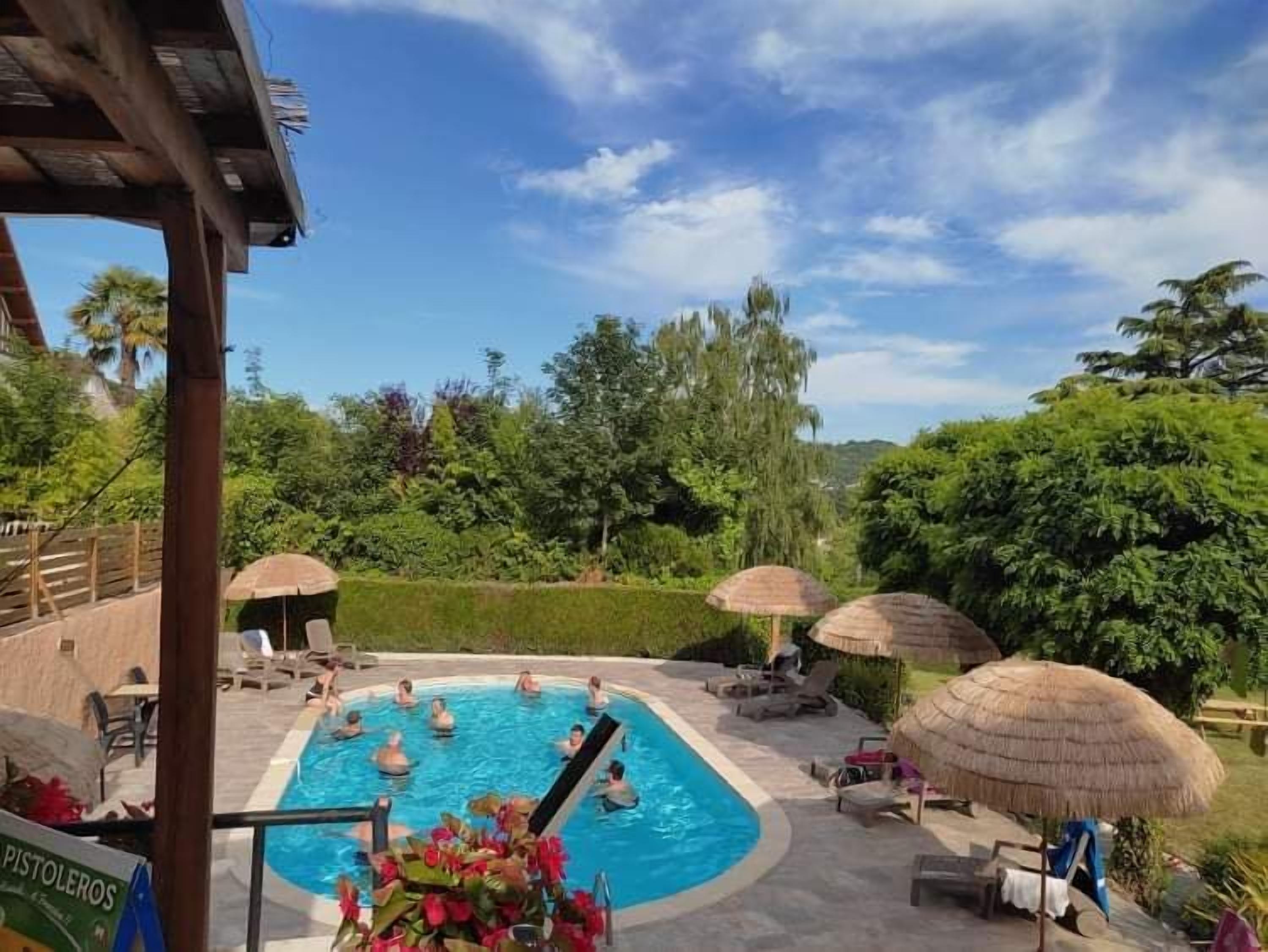 Ein Schwimmbecken mit Liegestühlen und Sonnenschirmen, umgeben von viel Grün.