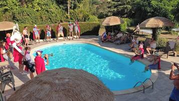 A swimming pool surrounded by lounge chairs and umbrellas, with people relaxing and some playing musical instruments.