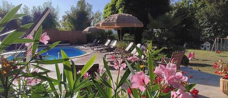 A pool area with lounge chairs, a thatched umbrella, and tropical plants.